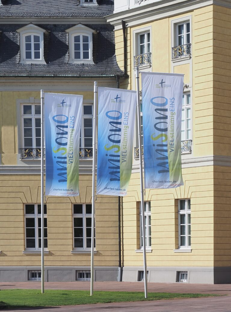 Drei Werbefahnen mit Logo und Auslegerkonfektion wehen vor dem Karlsruher Schloss