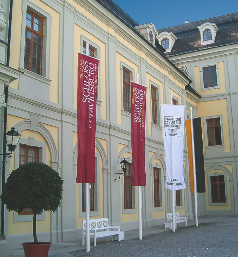 Drei Fahnenmasten mit gehissten Bannerfahnen vor einem Schloss